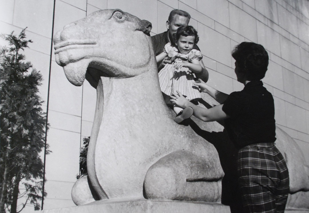Black and white photograph of two parents and a child atop the iconic Asian Art Museum camel 